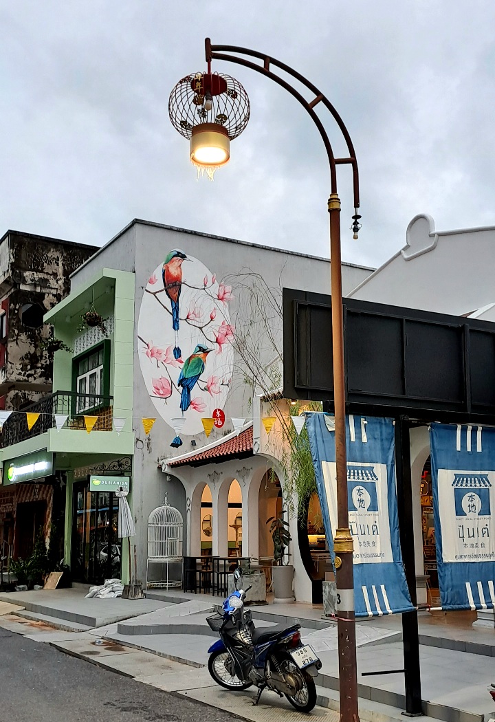 Photo de la ville de Phuket avec un lampdaire aux inspirations chinoises et un dessin d'un oiseau et de fleurs de cerisier sur un bâtiment