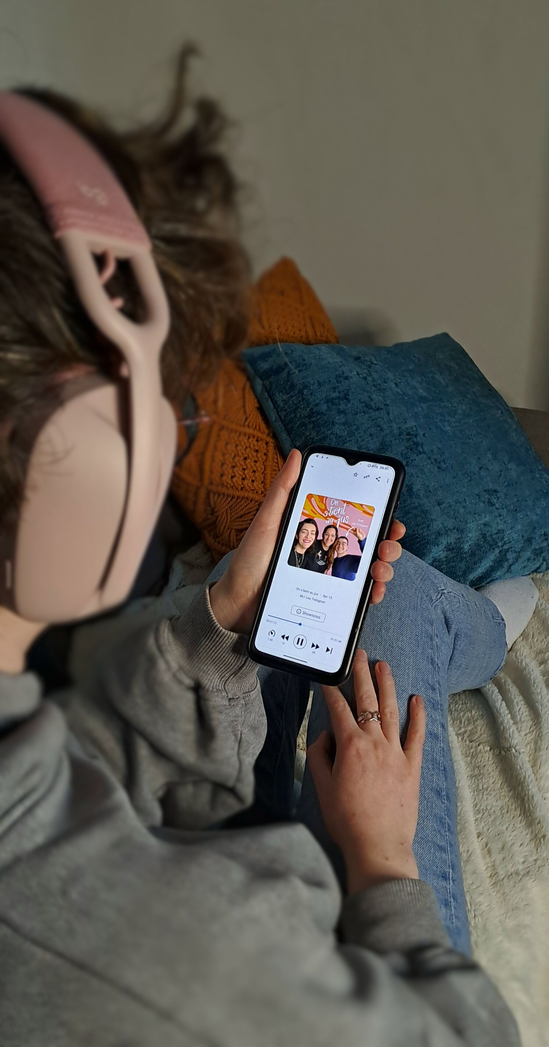 Photo de moi assise sur un canapé en train d'écouter le podcast avec un casque rose sur les oreilles